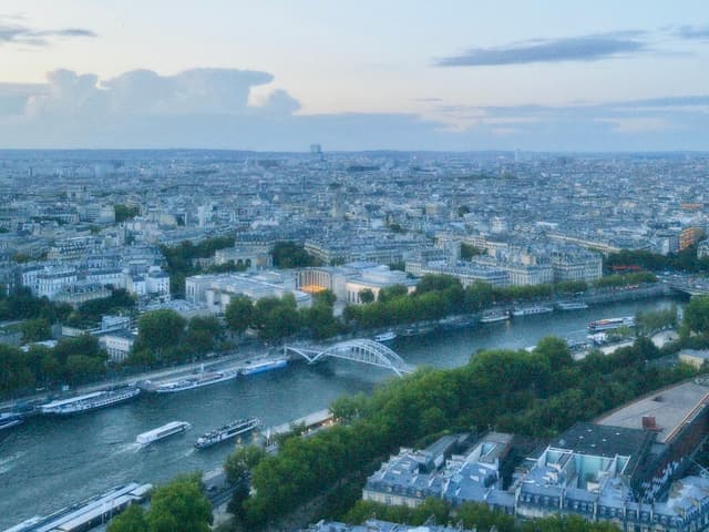 aerial view of the seine river in paris at dusk with boats, green trees, stone bridges, and city buildings under blue light