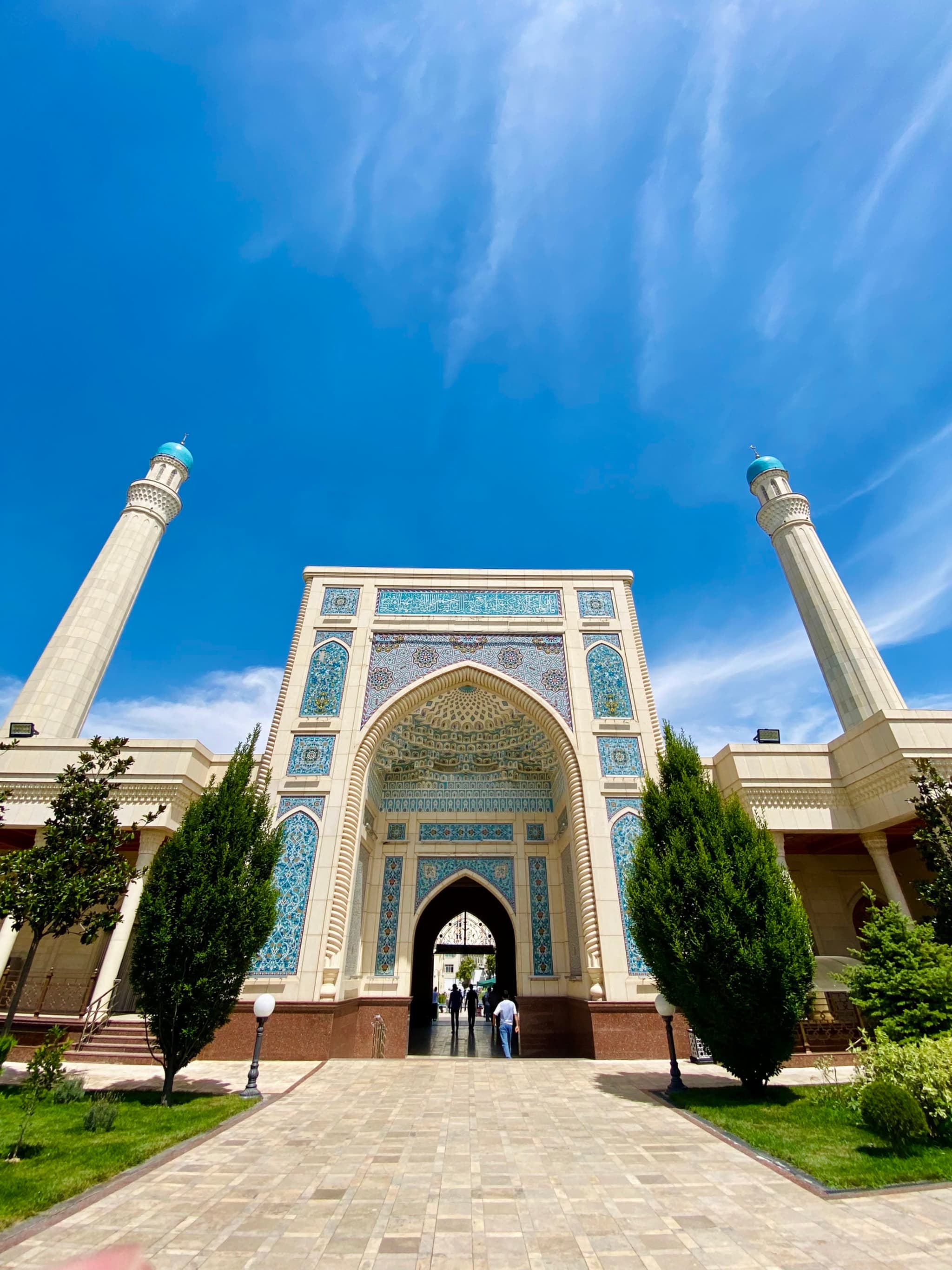 Majestic mosque entrance with intricate blue tilework and tall minarets under a vibrant sunny sky, creating a serene and architectural atmosphere