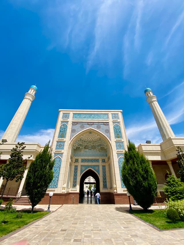 Majestic mosque entrance with intricate blue tilework and tall minarets under a vibrant sunny sky, creating a serene and architectural atmosphere