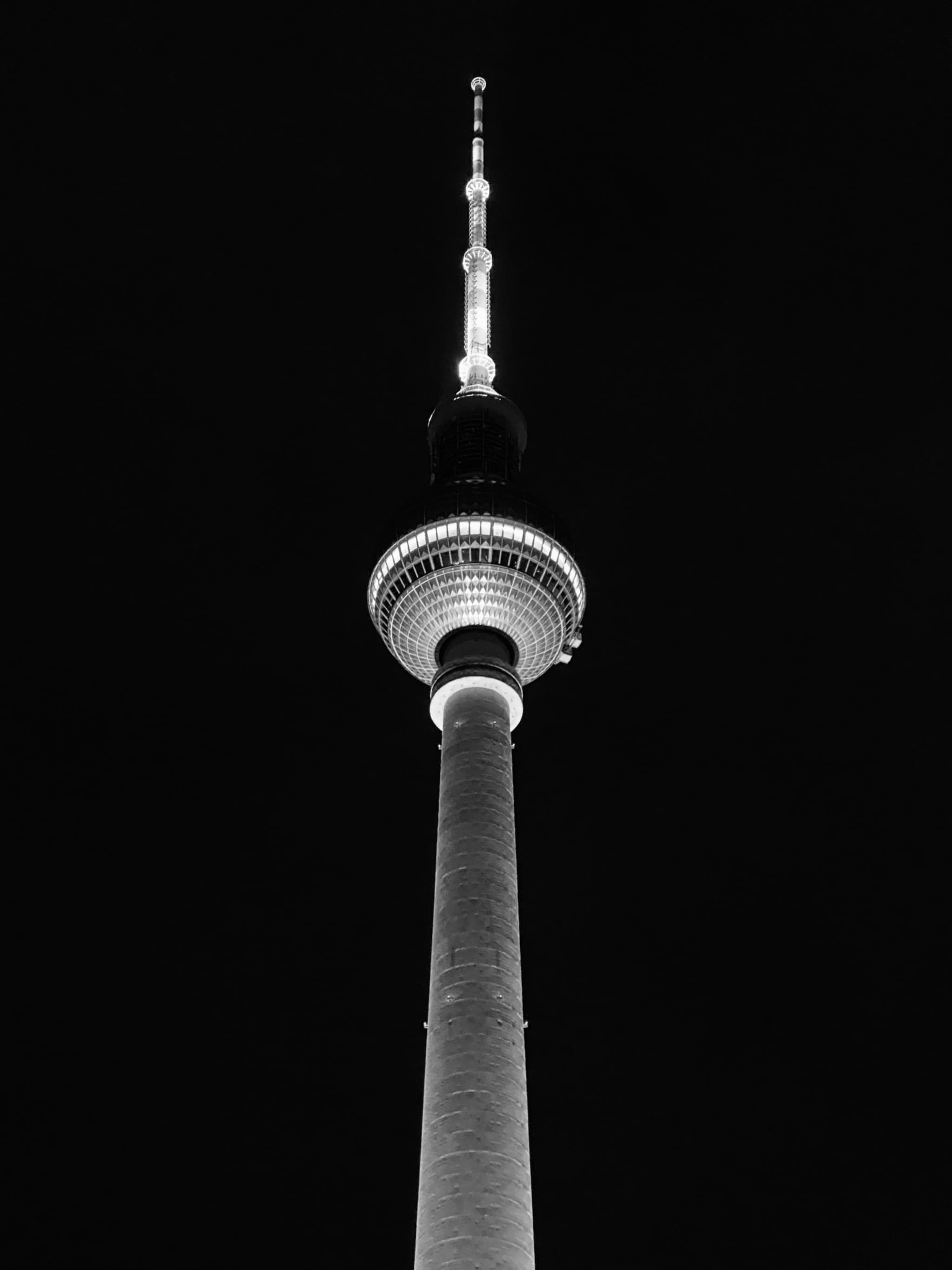 berlin tv tower illuminated at night, captured from a low angle against a dark sky in high contrast black and white photography