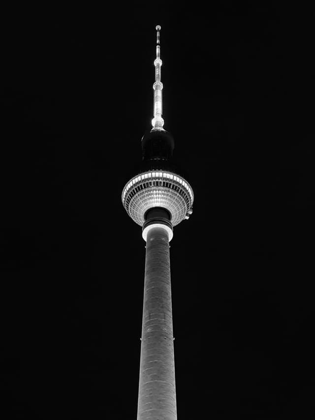 berlin tv tower illuminated at night, captured from a low angle against a dark sky in high contrast black and white photography