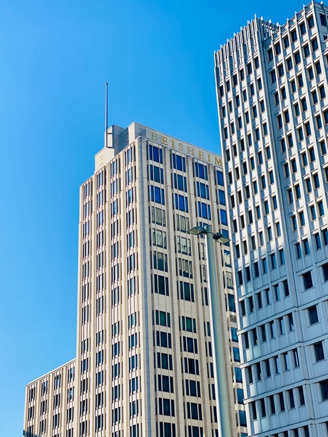 tall concrete office buildings rise against a clear blue sky under bright daylight, showing geometric window patterns and modern urban architecture