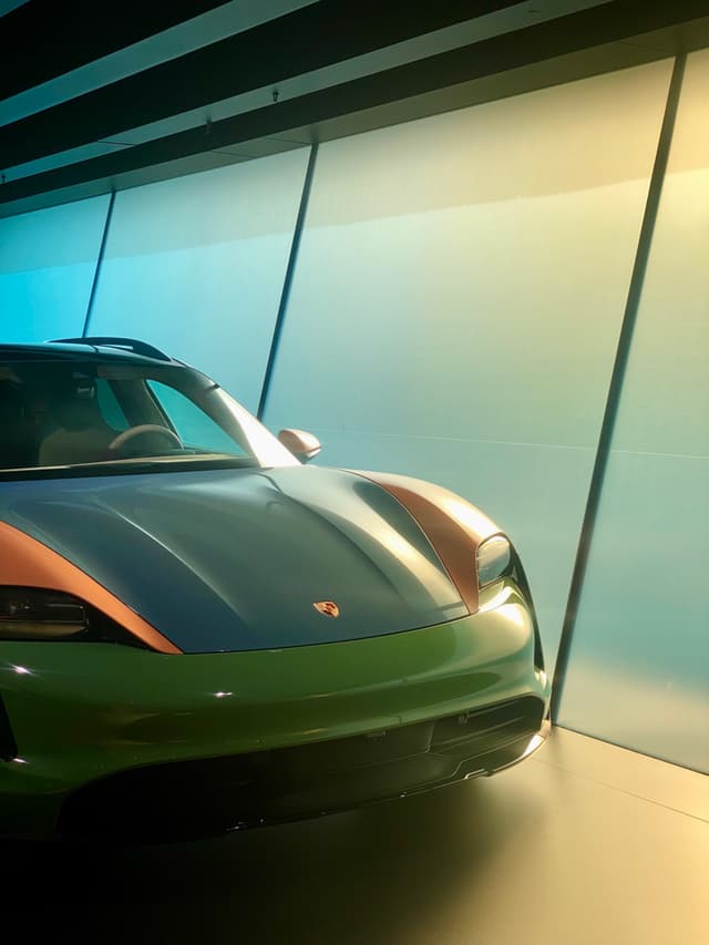 multicolored porsche taycan parked inside a modern showroom with large glass windows and soft gradient lighting reflecting off the metallic car hood