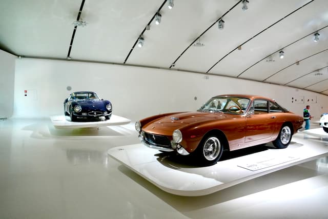vintage copper and dark blue sports cars displayed on white platforms inside a modern museum with bright overhead track lighting