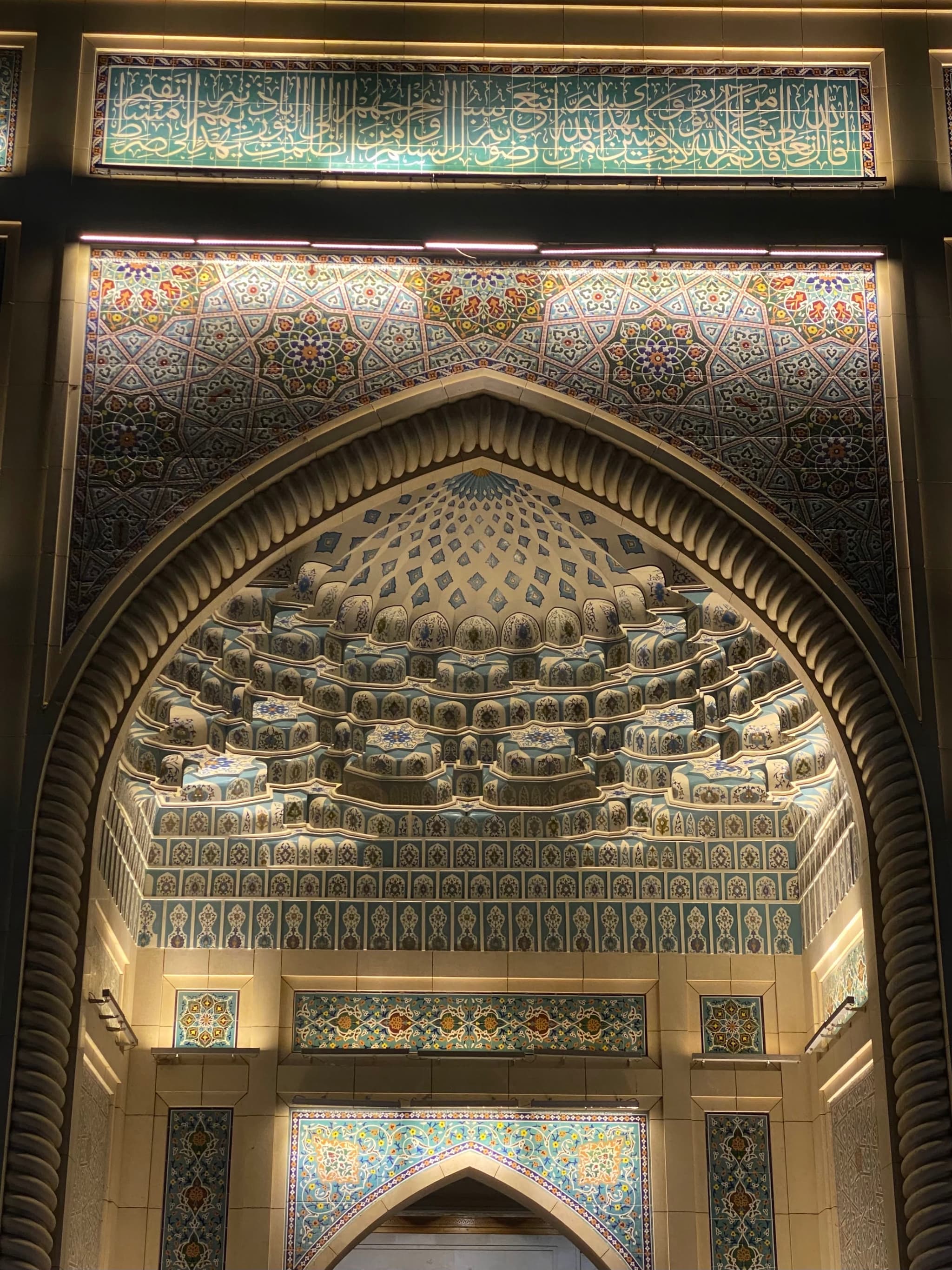 intricate tile patterns decorate the arched stone entrance of a mosque at night, illuminated by warm lights highlighting the detailed geometric carvings
