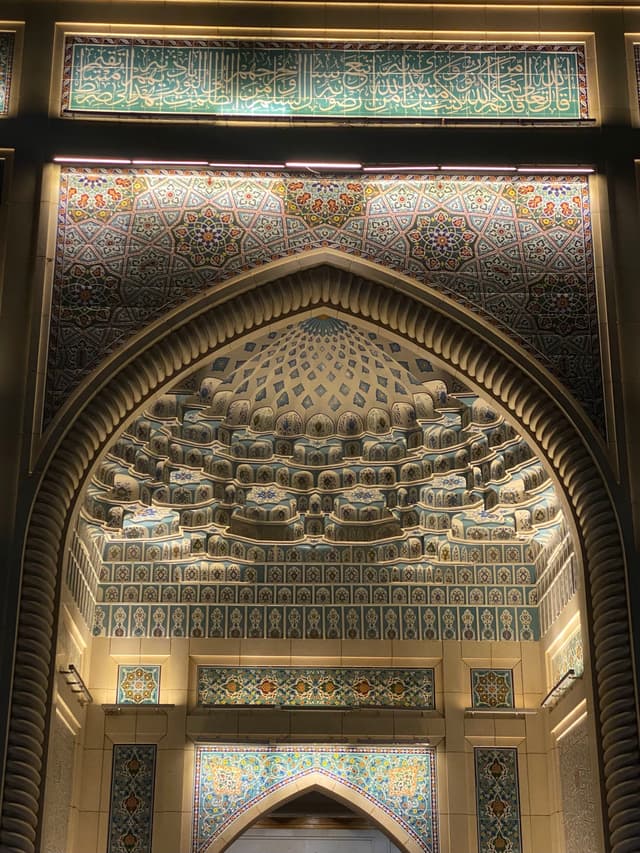 intricate tile patterns decorate the arched stone entrance of a mosque at night, illuminated by warm lights highlighting the detailed geometric carvings