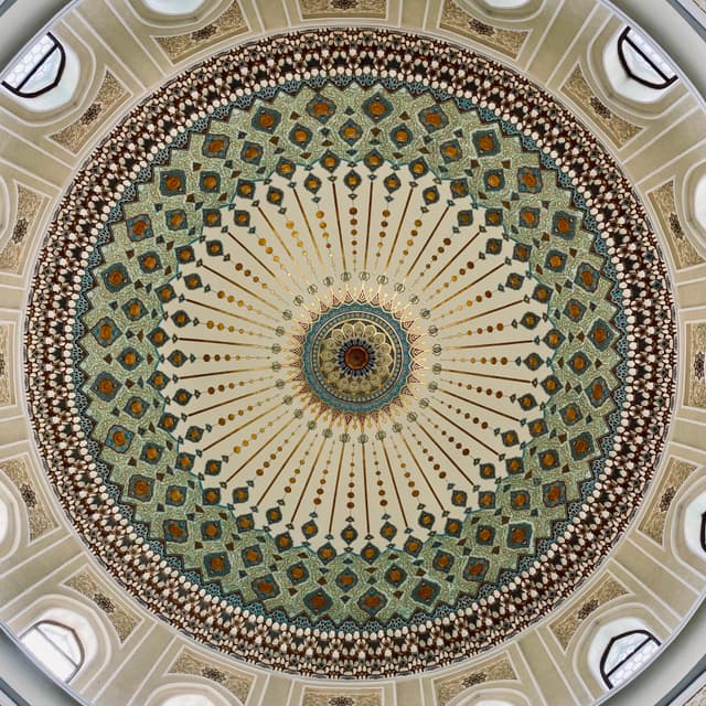 symmetrical view of an ornate mosque dome featuring intricate geometric patterns, soft daylight, and circular architectural details in a quiet interior space