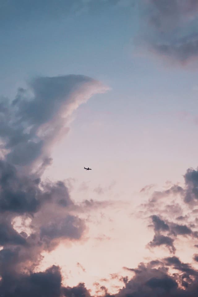 small airplane flying through a vast sky with purple clouds during sunset, captured from below in a quiet, wide-angle landscape shot