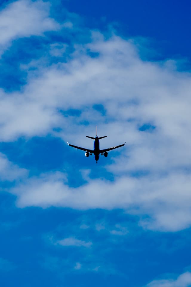 commercial airplane flying upward through a bright blue sky with scattered white clouds during the day, captured from a low ground angle