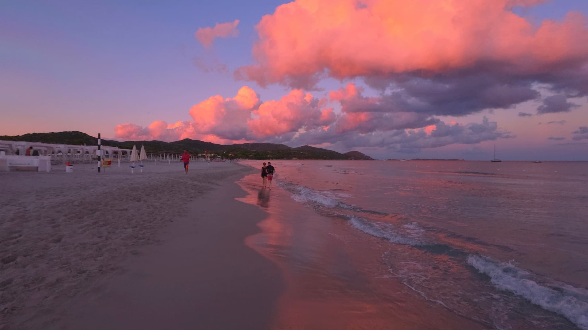 pink sunset clouds reflect on wet sand along a quiet beach with distant hills under a darkening purple sky at dusk