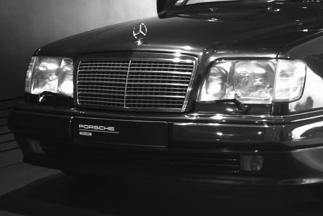 front view of a black mercedes-benz 500e in a dark studio, highlighting the chrome grille and headlights under sharp overhead lighting