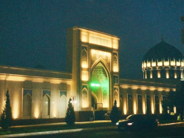 illuminated mosque facade at night with warm spotlights, arched entrance, and a central dome against a dark blue evening sky in uzbekistan
