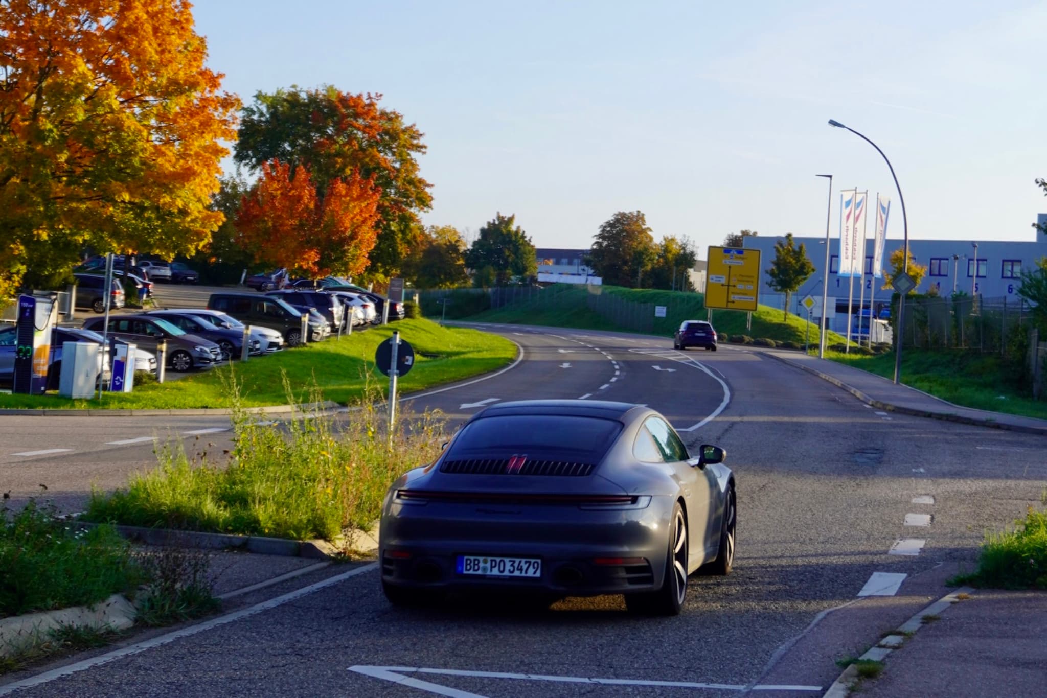dark grey porsche parked on an asphalt road during a sunny autumn afternoon with orange trees and a distant parking lot