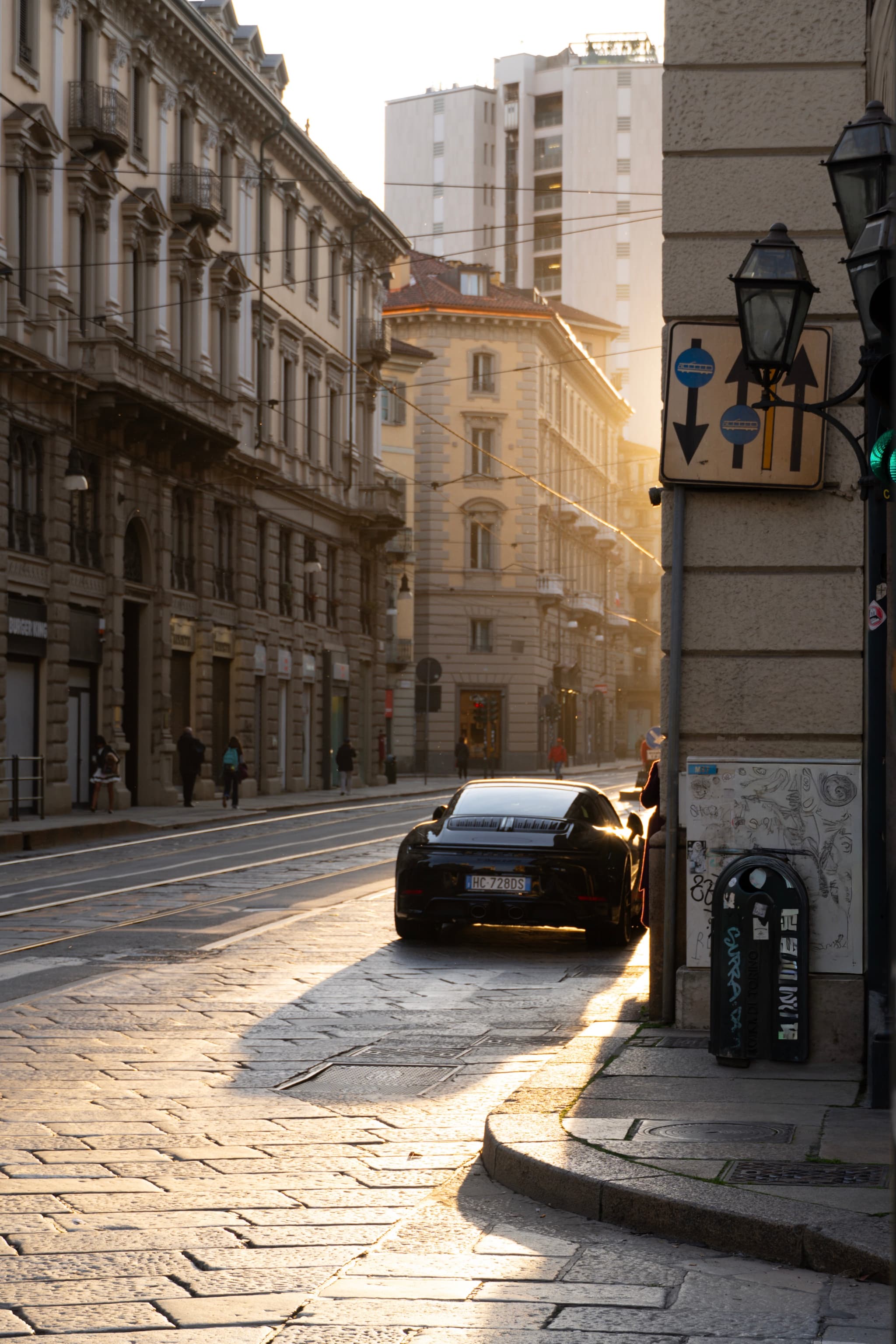 black sports car parked on a cobblestone street in milan at sunset with warm light hitting historic buildings and urban traffic signs