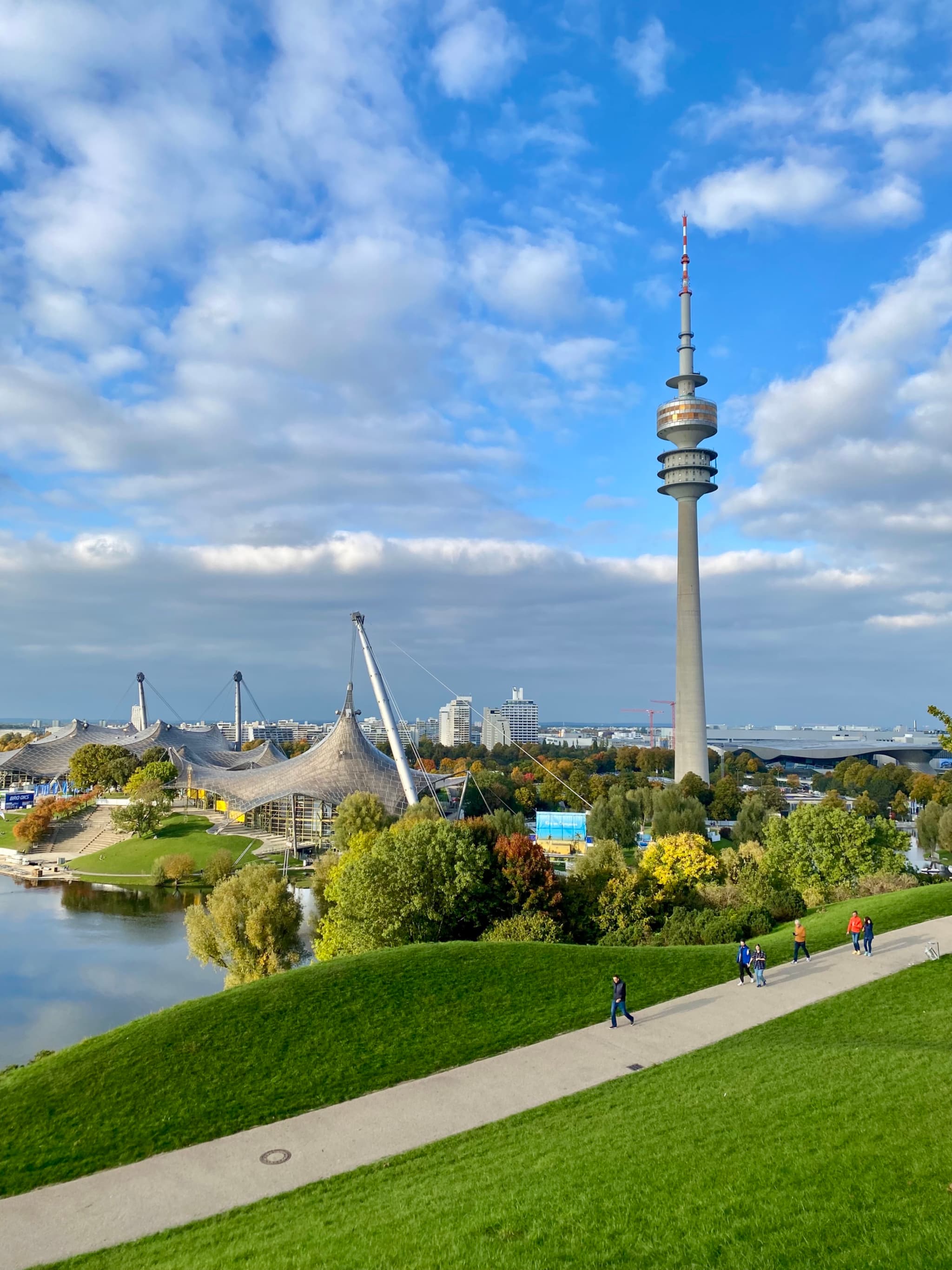 olympic tower and stadium in munich under a bright blue sky with green hills and walking paths on a clear autumn day