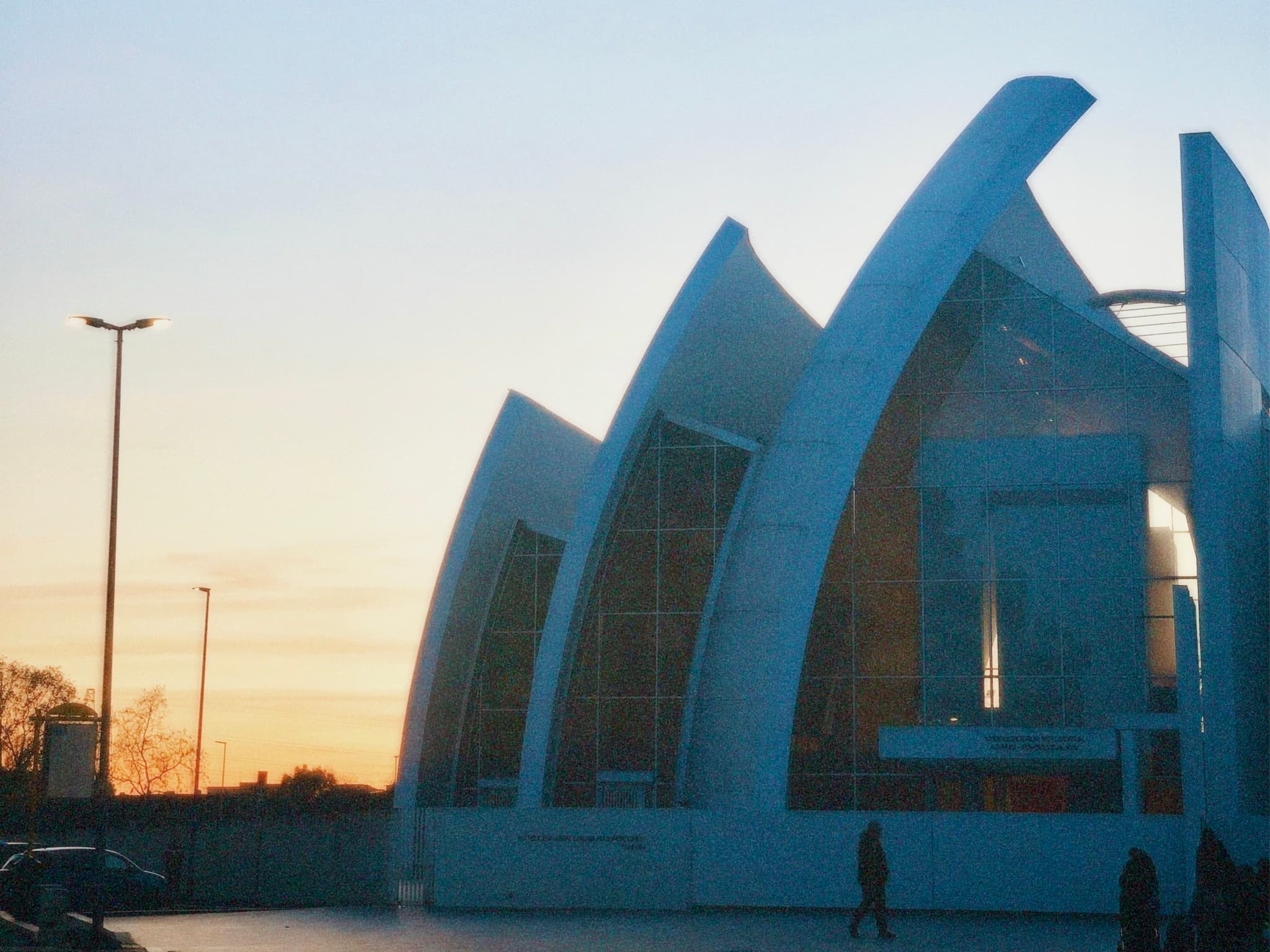 modern church building with curved white concrete arches stands against a clear sunset sky in a quiet suburban parking lot area