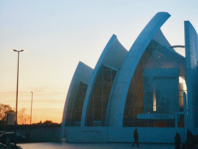 modern church building with curved white concrete arches stands against a clear sunset sky in a quiet suburban parking lot area