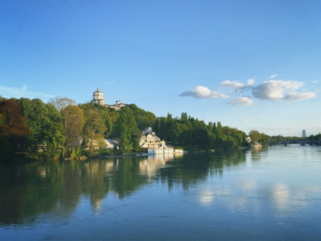 turin cityscape with the monte dei cappuccini church reflecting in the po river under a clear blue sky during late afternoon light