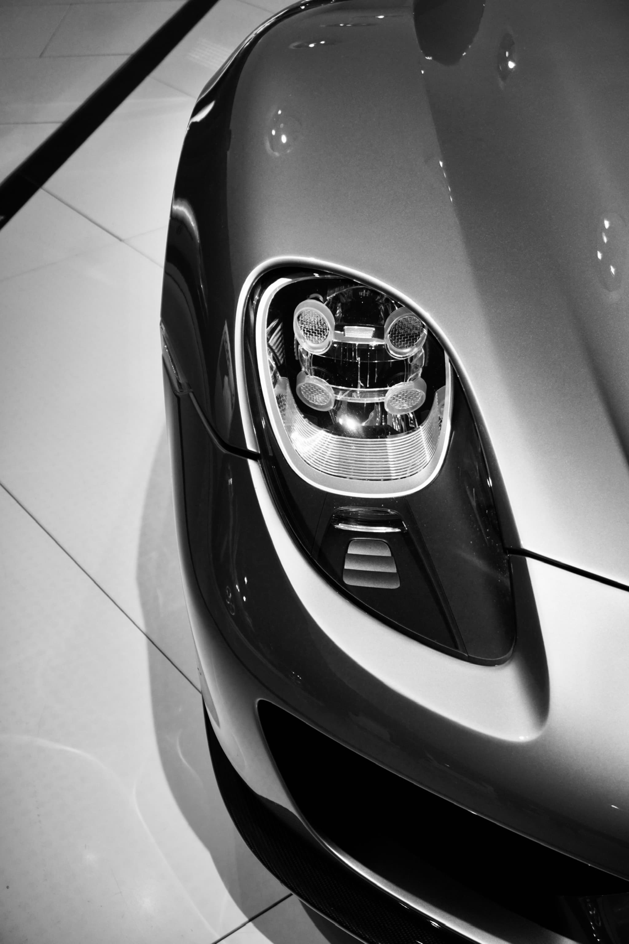 close-up of a porsche headlight in a showroom with high-contrast lighting, showing metallic curves and technical design on a white floor