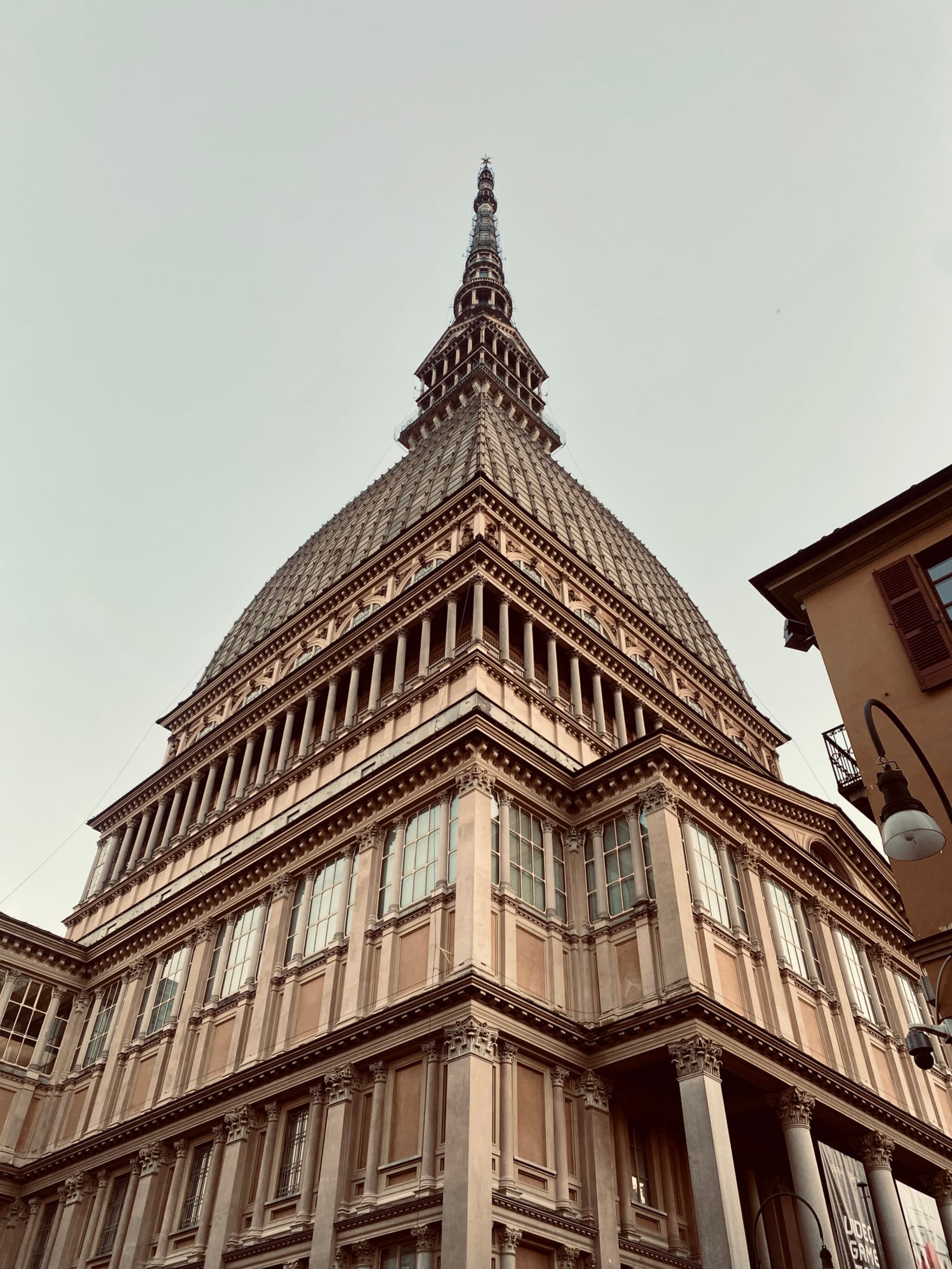 low angle view of the mole antonelliana in turin under a grey sky with detailed stone architecture and a street lamp nearby