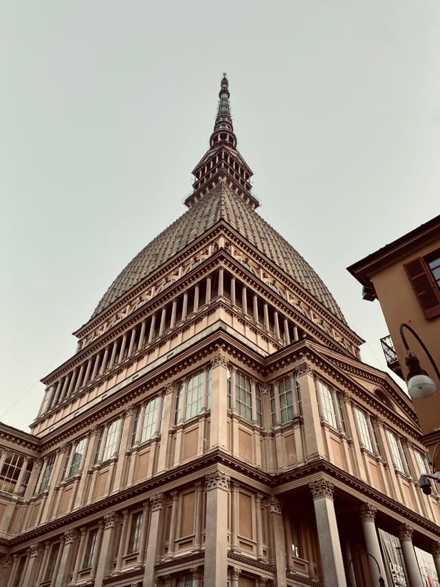low angle view of the mole antonelliana in turin under a grey sky with detailed stone architecture and a street lamp nearby