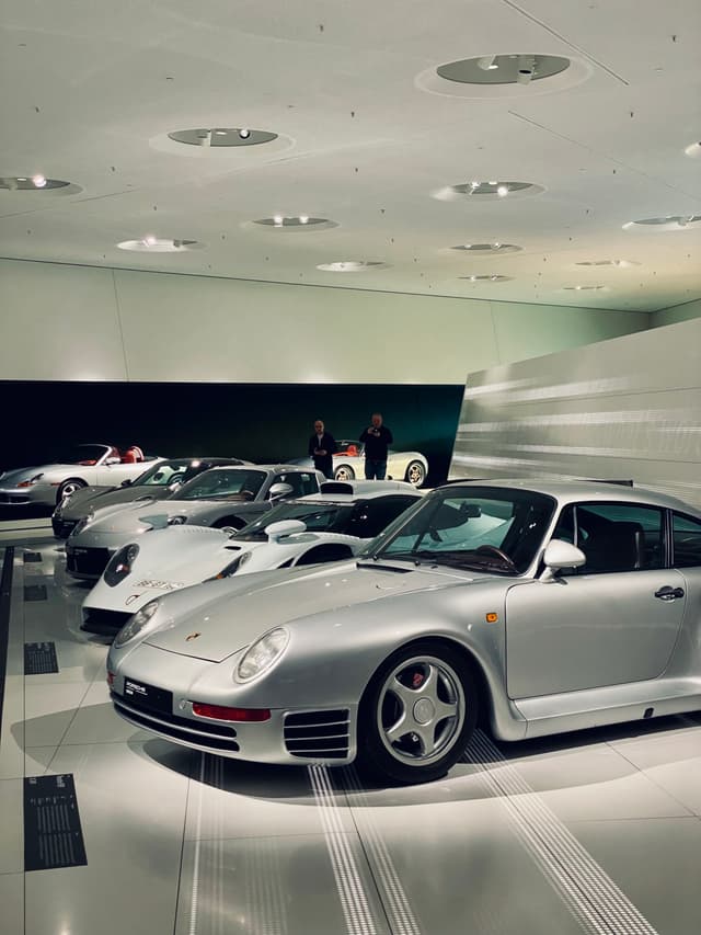 silver porsche sports cars parked in a bright modern museum gallery with overhead recessed lighting and white tiled floors on display