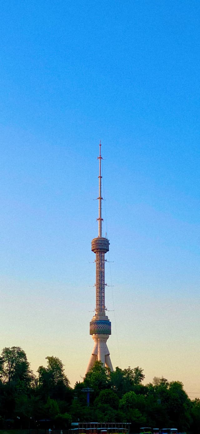 tashkent tv tower rises above green trees against a clear blue sky during late afternoon light in the city of tashkent