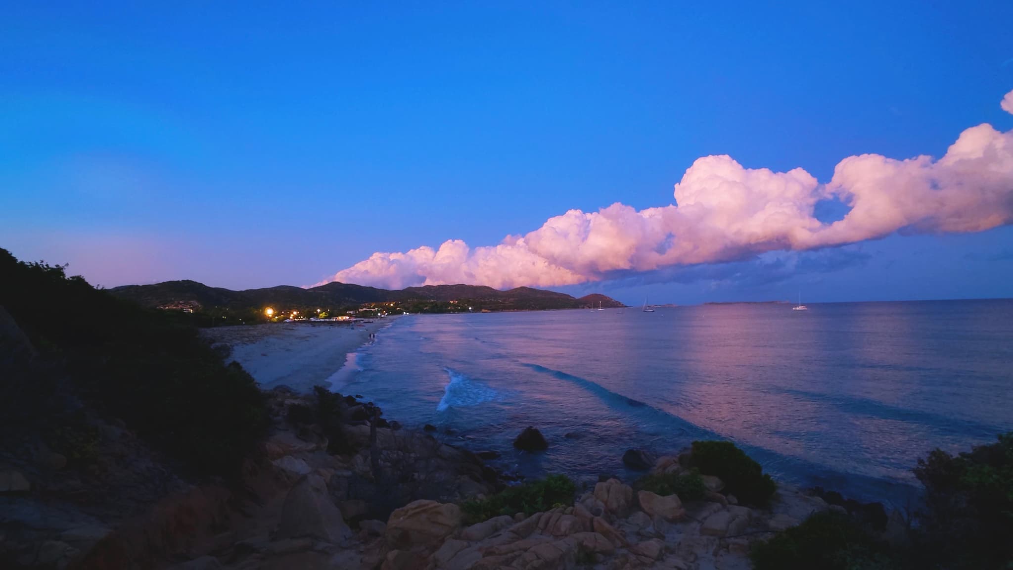 pink clouds hover over a dark coastline at twilight, reflecting light onto the calm ocean water near a quiet beach in st. lucia