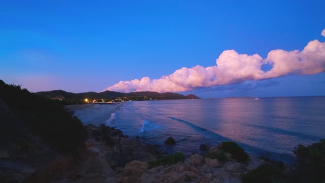 pink clouds hover over a dark coastline at twilight, reflecting light onto the calm ocean water near a quiet beach in st. lucia