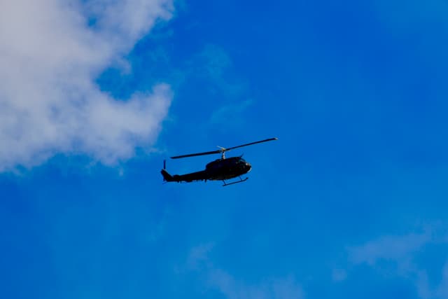 military helicopter silhouette flying against a bright blue sky with white clouds during a clear day in a low angle view