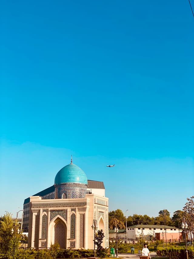blue dome of the tilla sheikh mosque in tashkent under a clear sky with a small airplane flying overhead in bright daylight