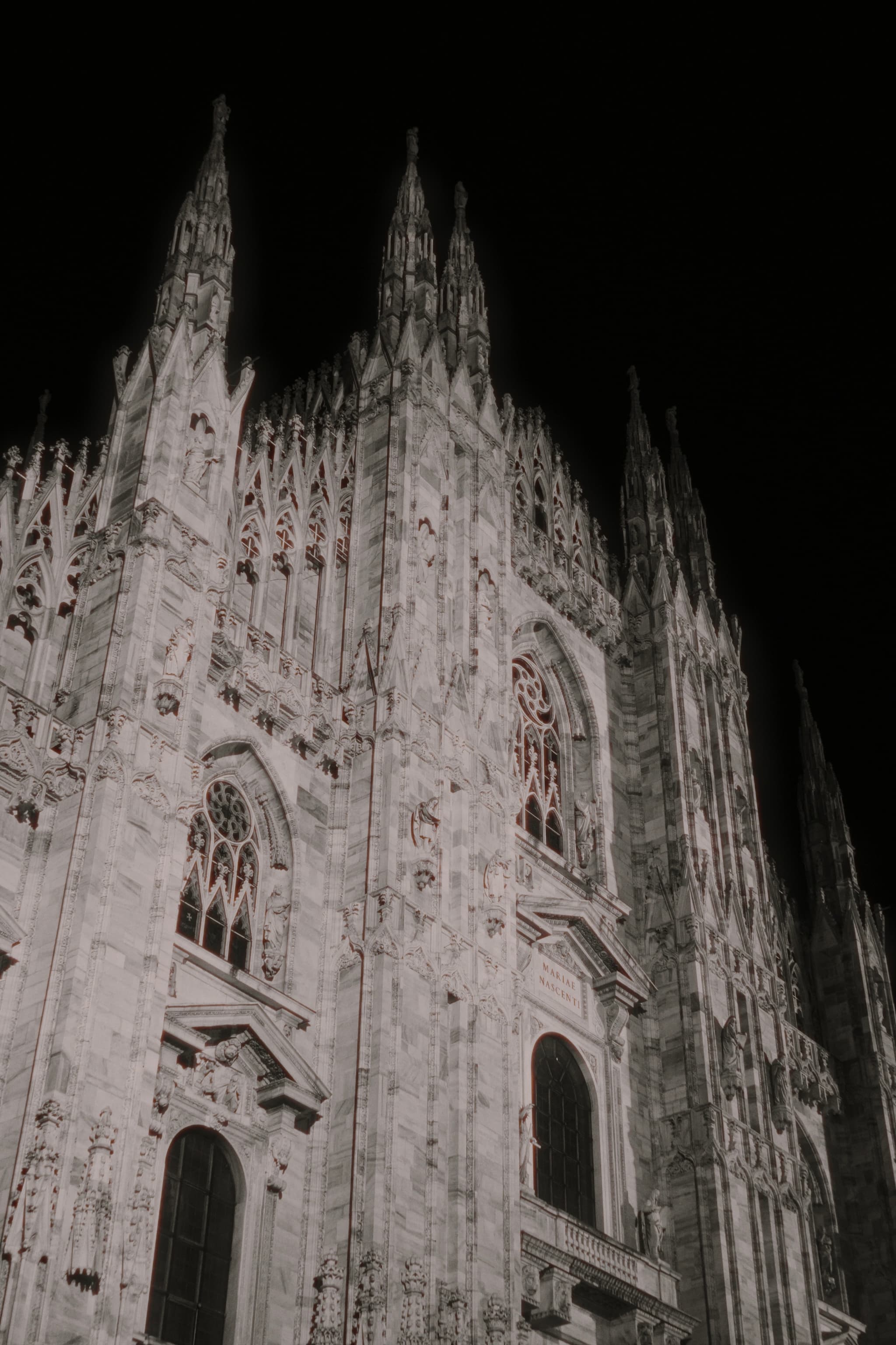 low angle view of milan cathedral facade at night with bright artificial lighting highlighting the intricate marble carvings and gothic spires
