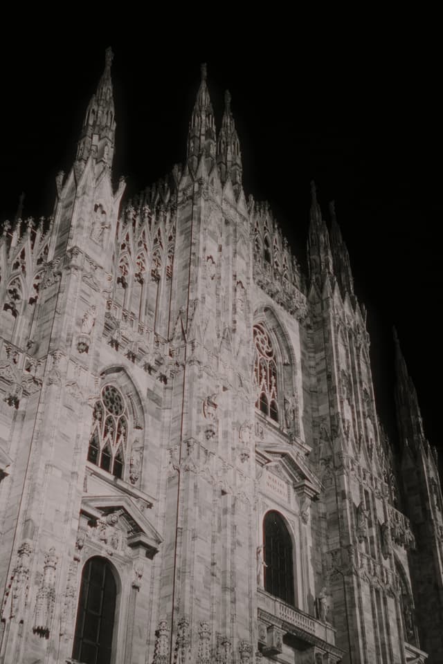 low angle view of milan cathedral facade at night with bright artificial lighting highlighting the intricate marble carvings and gothic spires