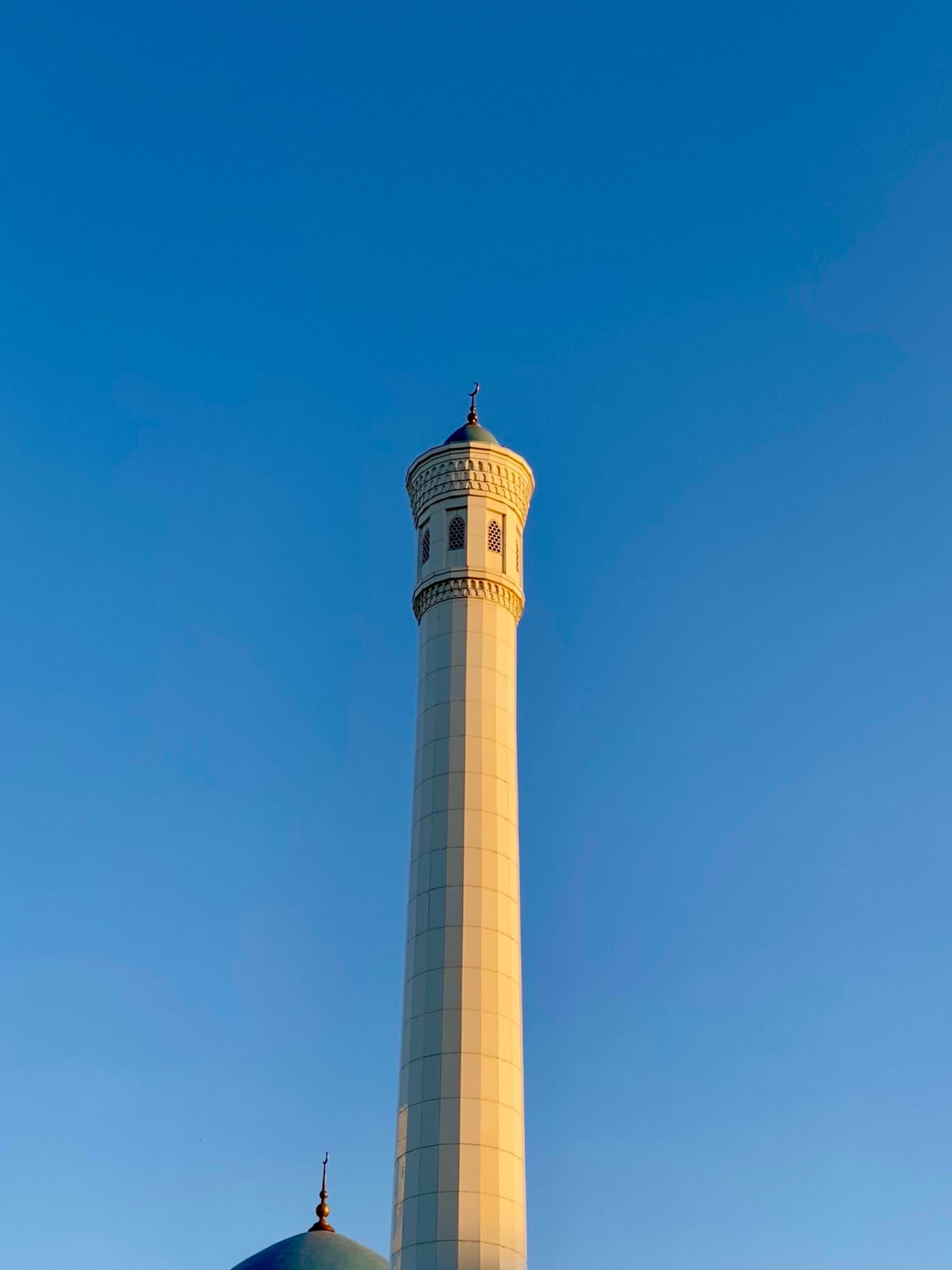 tall stone minaret against a clear blue sky, captured in bright daylight with sharp shadows and architectural detail on the tower top