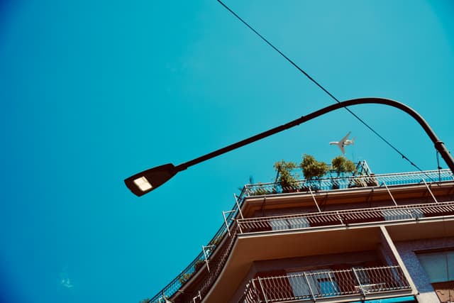 a bright street lamp illuminates the corner of a brown building against a clear blue sky during the sunny day