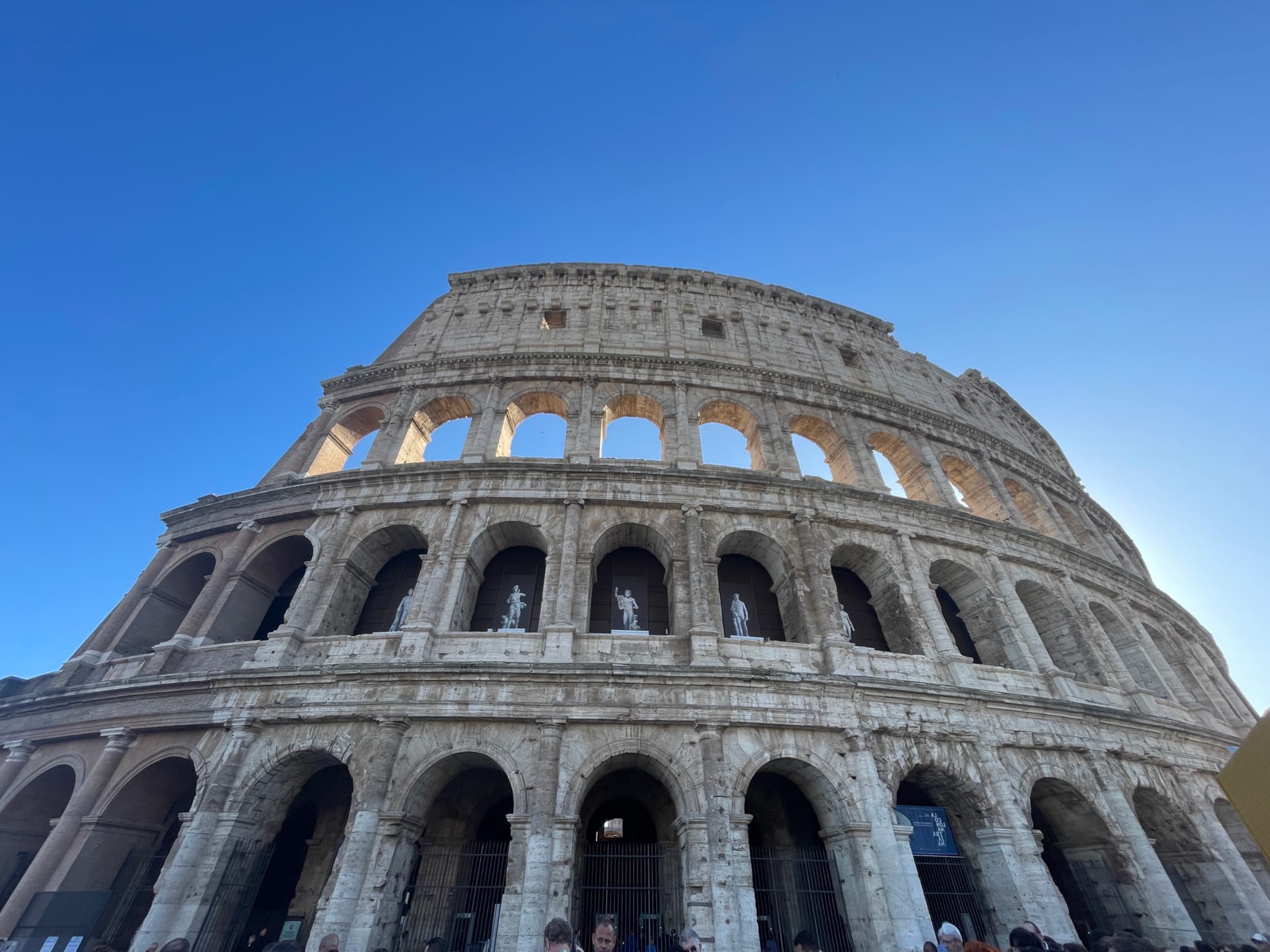 low angle view of the stone colosseum in rome under a clear blue sky during bright daylight with visible arched exterior levels