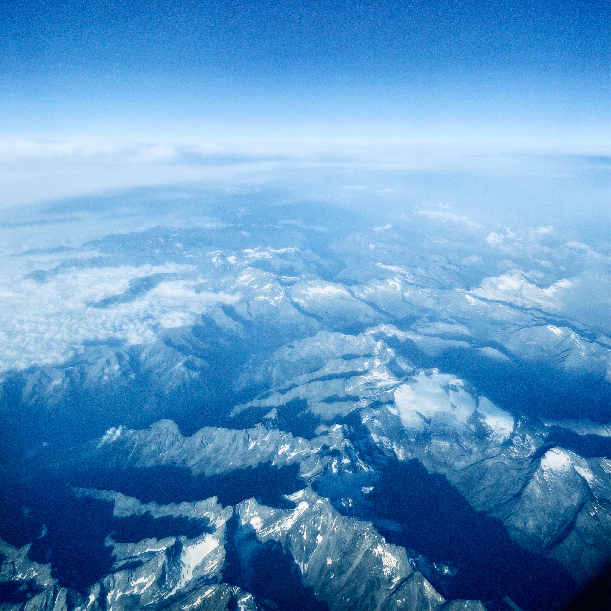 Aerial view of snow-capped mountain peaks under a clear blue sky, capturing a serene, expansive landscape with bright, natural daylight and shadows