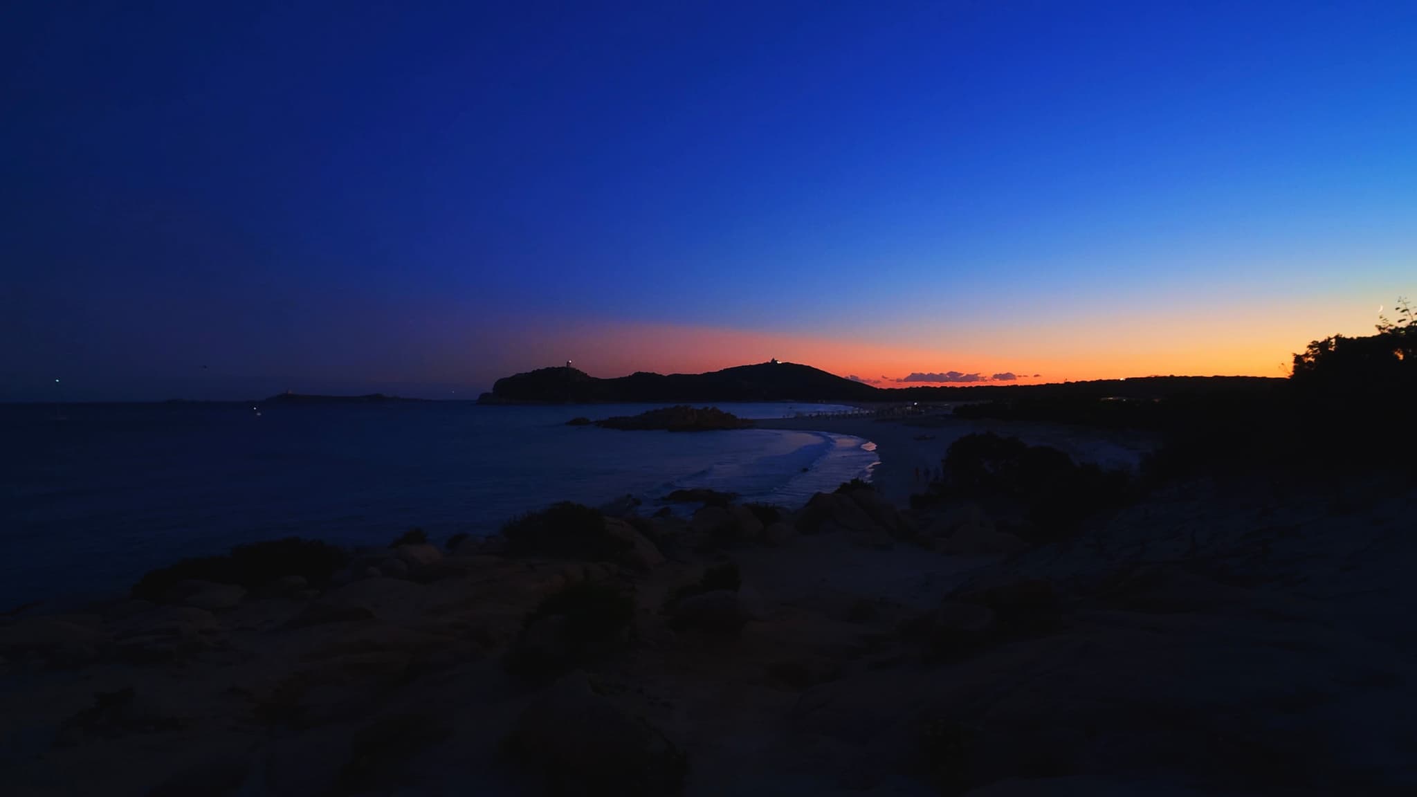 dark blue twilight sky over a calm ocean bay with a distant rocky coastline and orange horizon glow at dusk