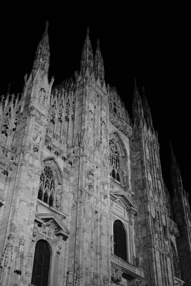 low angle view of the milan cathedral facade at night, featuring gothic stone spires lit by artificial light in black and white