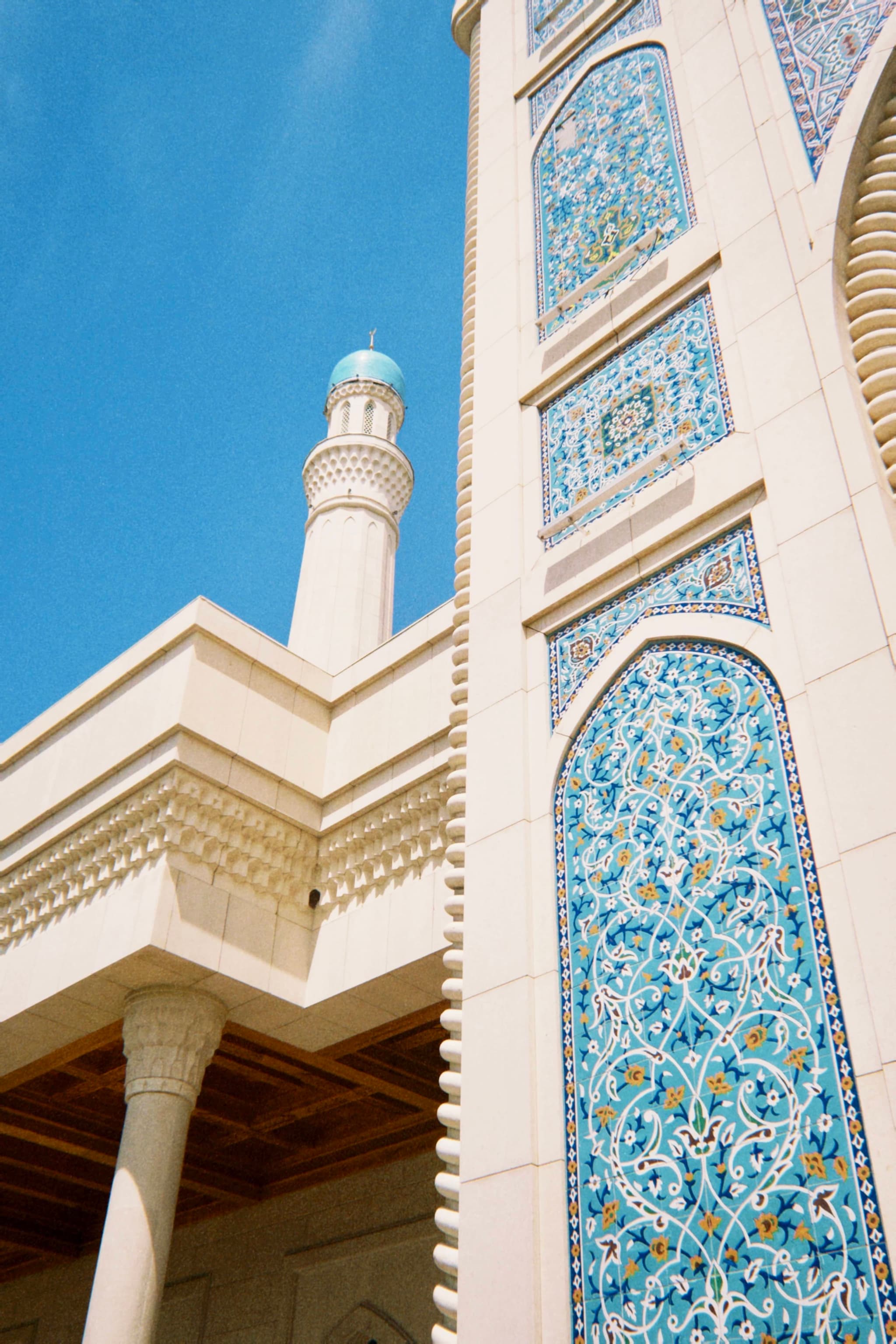 blue tile mosaics decorate the stone facade of a mosque under bright sunlight with a clear sky and a single minaret visible