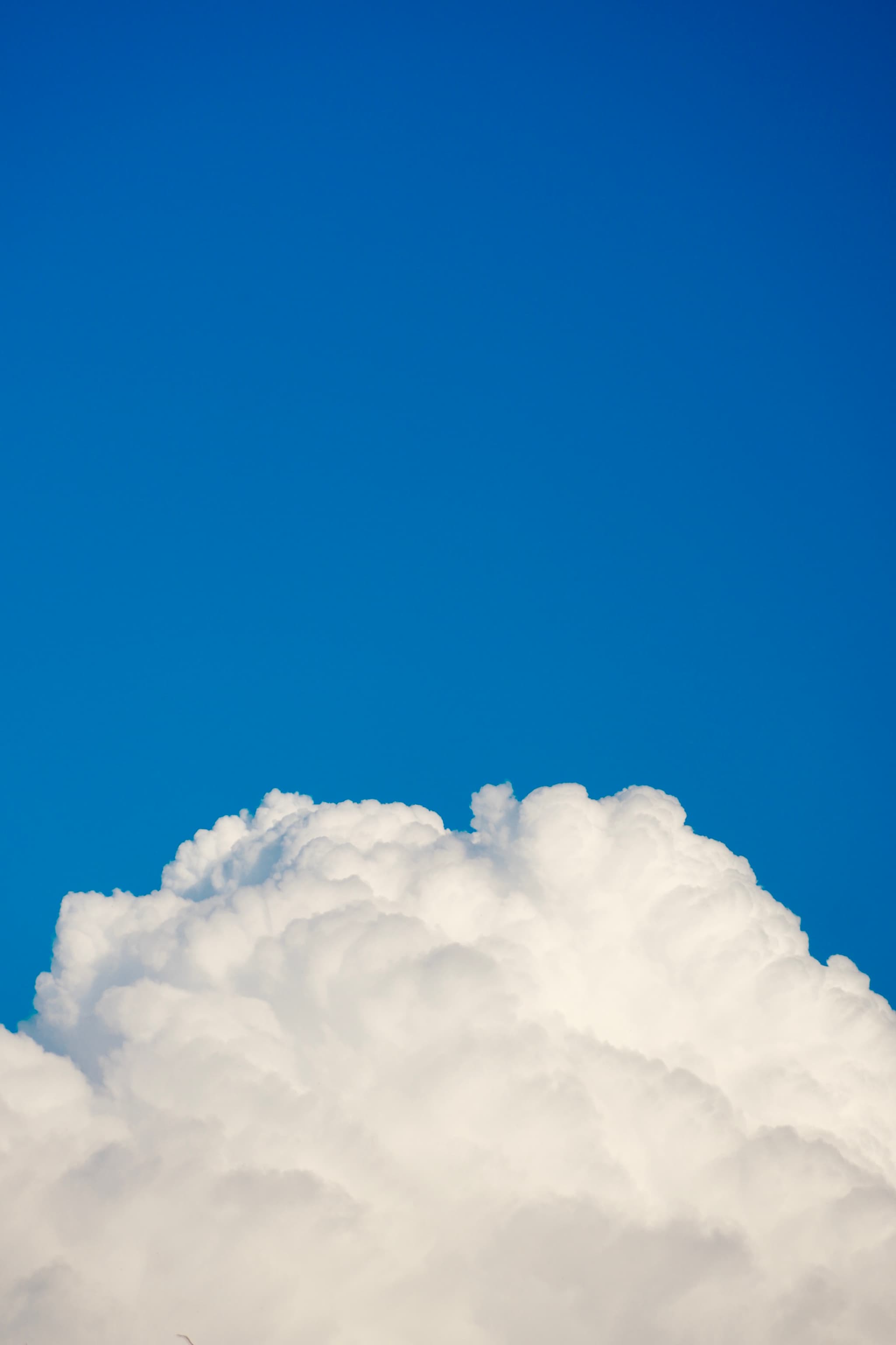 a single white cumulus cloud rises against a clear blue sky under bright daylight, capturing a simple and open outdoor view