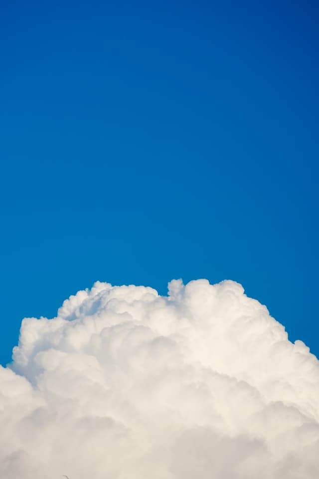 a single white cumulus cloud rises against a clear blue sky under bright daylight, capturing a simple and open outdoor view