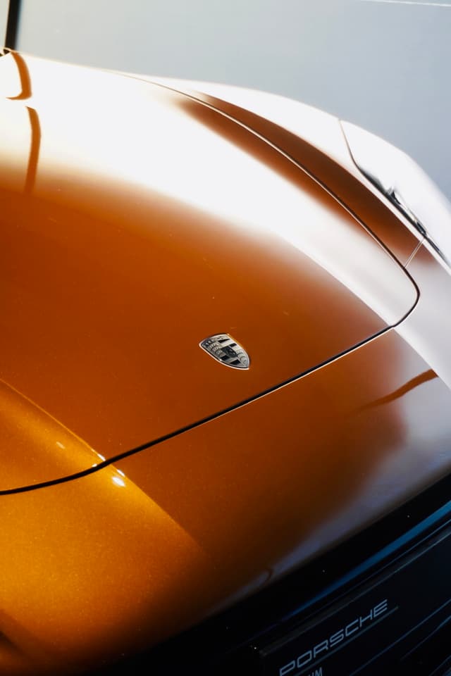 close-up of a metallic orange porsche hood with the emblem visible under bright studio lighting in a clean garage setting