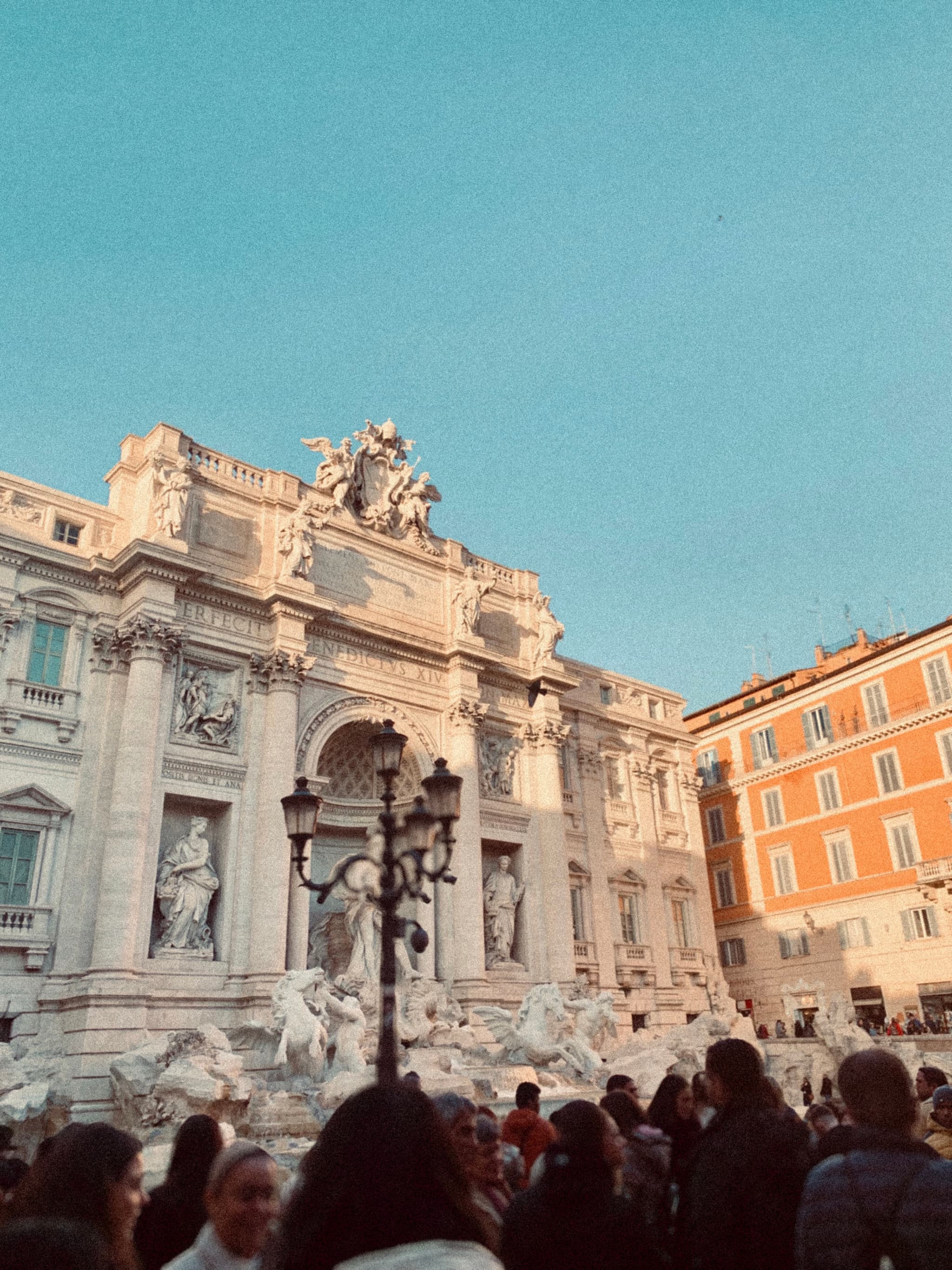 trevi fountain in rome during late afternoon with golden light hitting the stone facade and a crowd of tourists in the foreground