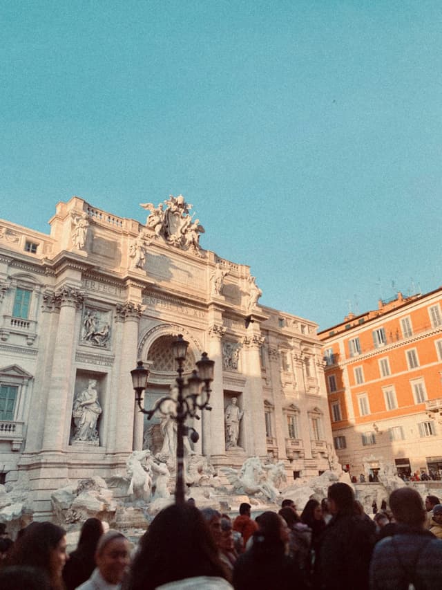 trevi fountain in rome during late afternoon with golden light hitting the stone facade and a crowd of tourists in the foreground