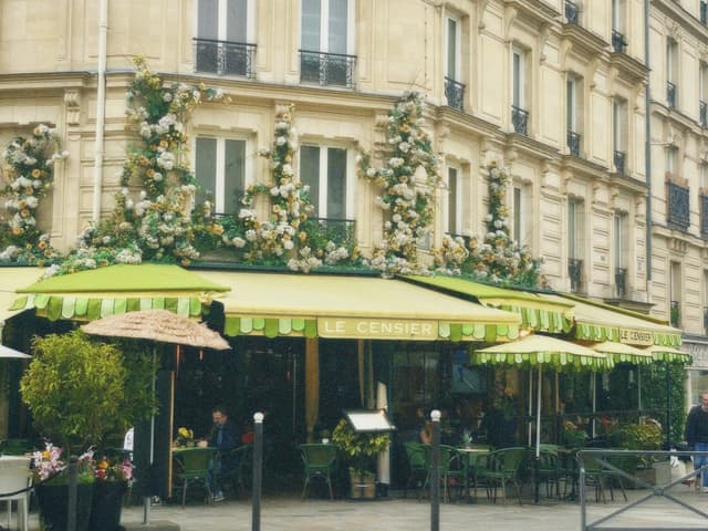 green striped awnings shade a sidewalk cafe in paris with floral decorations on the limestone facade under soft daylight on a quiet street