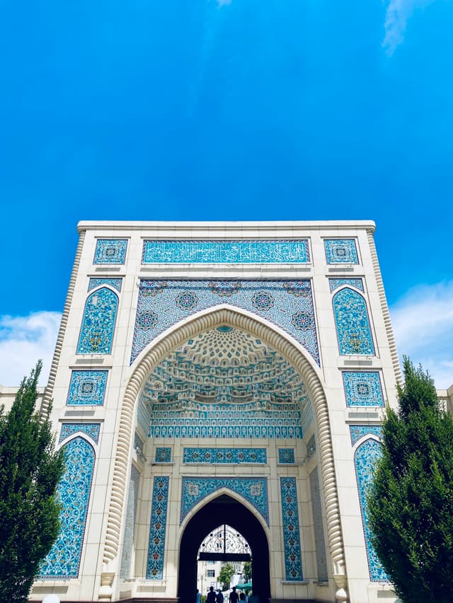 blue tiled archway of a mosque under a clear sky with green cypress trees in bright daylight, architectural photography of uzbekistan