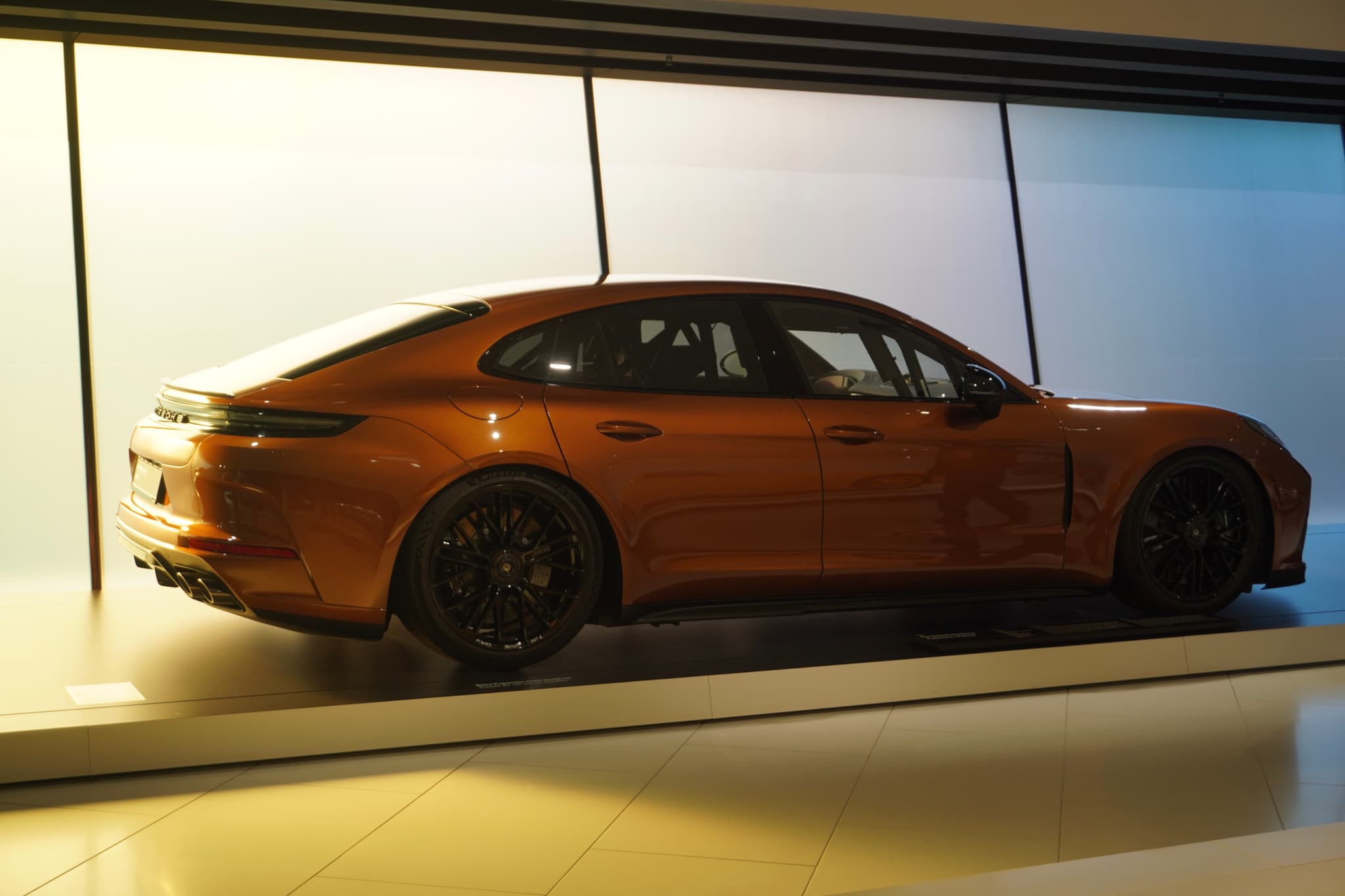 copper porsche panamera parked in a minimalist showroom with bright backlighting, showcasing the sleek profile and dark wheels on a clean floor