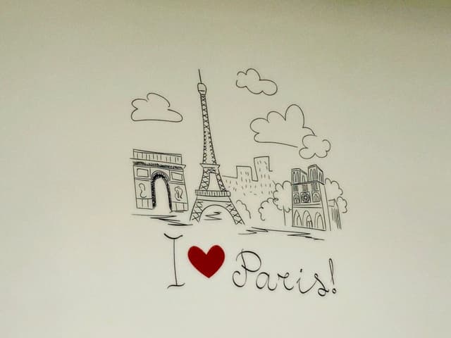 black ink drawing of eiffel tower and paris landmarks on a plain wall with a red heart icon and handwritten text
