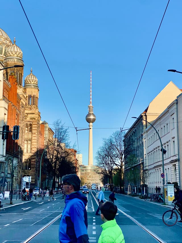 berlin tv tower rises above a city street with pedestrians crossing under clear blue sky during a bright afternoon in germany